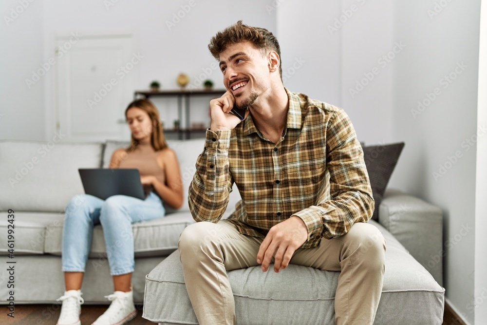 Young hispanic couple smiling happy using laptop and smartphone sitting on the sofa at home. Young hispanic couple smiling happy using laptop and smartphone sitting on the sofa at home.