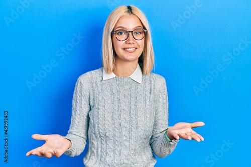 Foto Beautiful blonde woman wearing glasses clueless and confused expression with arms and hands raised