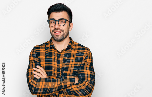 Hispanic man with beard wearing casual clothes and glasses happy face smiling with crossed arms looking at the camera. positive person. © Krakenimages.com