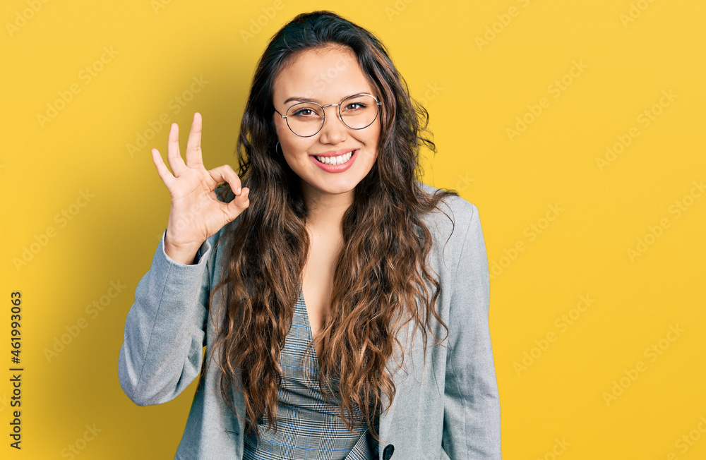 Young hispanic girl wearing business clothes and glasses smiling positive doing ok sign with hand and fingers. successful expression. Young hispanic girl wearing business clothes and glasses smiling positive doing ok sign with hand and fingers. successful expression.