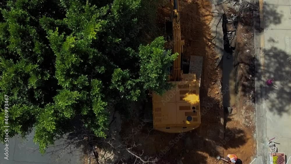 Aerial view of an excavator digging on construction site under a tree Aerial view of an excavator digging on construction site under a tree