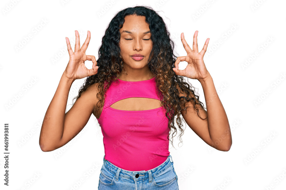 Young hispanic woman with curly hair wearing pink top relax and smiling with eyes closed doing meditation gesture with fingers. yoga concept. Young hispanic woman with curly hair wearing pink top relax and smiling with eyes closed doing meditation gesture with fingers. yoga concept.