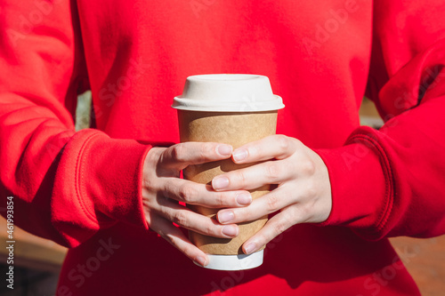 Woman's hands holds a disposable beige coffee cup in her hands.
