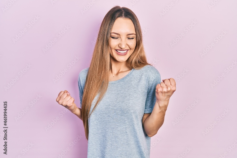 Young blonde girl wearing casual t shirt excited for success with arms raised and eyes closed celebrating victory smiling. winner concept. Young blonde girl wearing casual t shirt excited for success with arms raised and eyes closed celebrating victory smiling. winner concept.