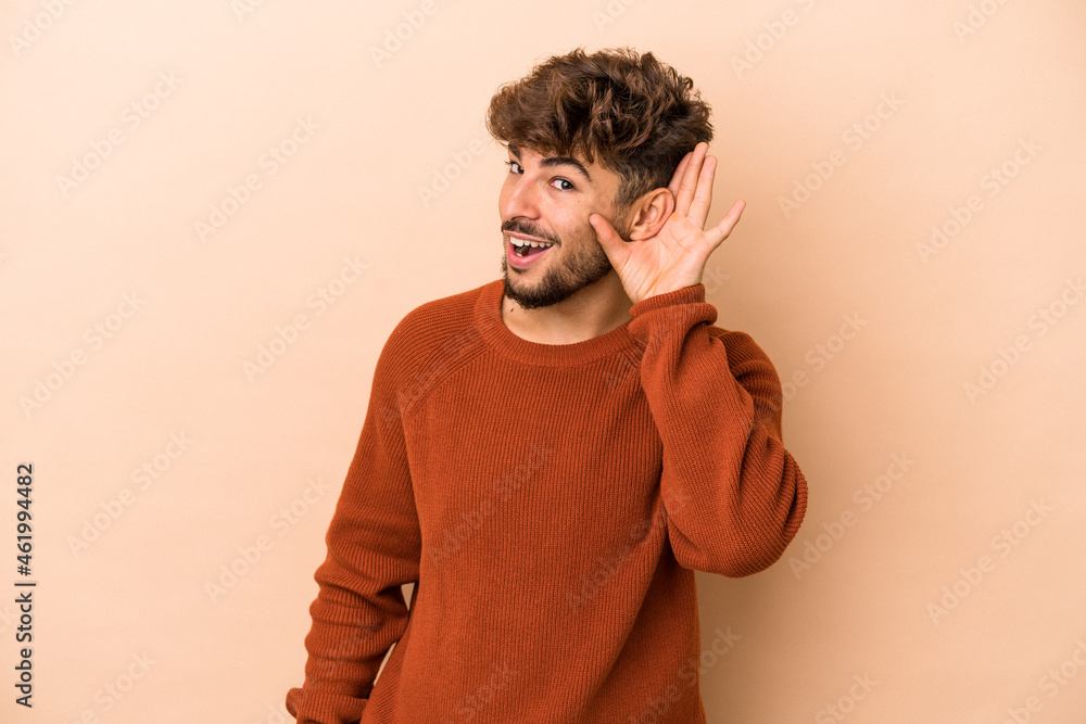 Young arab man isolated on beige background trying to listening a gossip. Young arab man isolated on beige background trying to listening a gossip.