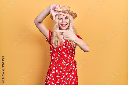 Beautiful caucasian woman with blond hair wearing summer hat smiling making frame with hands and fingers with happy face. creativity and photography concept. © Krakenimages.com
