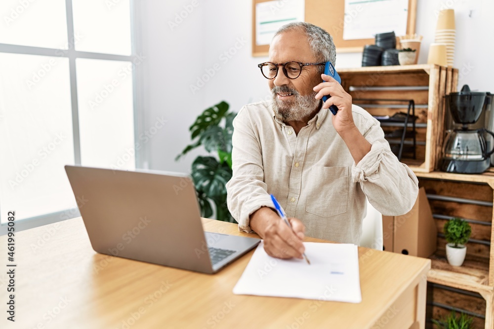 Senior grey-haired man talking on the smartphone working at office Senior grey-haired man talking on the smartphone working at office
