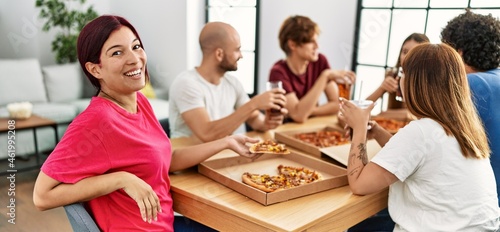 Group of young friends smiling happy eating italian pizza sitting on the table at home.