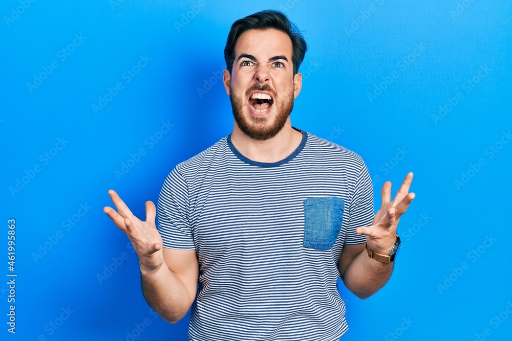 Handsome caucasian man with beard wearing casual striped t shirt crazy and mad shouting and yelling with aggressive expression and arms raised. frustration concept. Handsome caucasian man with beard wearing casual striped t shirt crazy and mad shouting and yelling with aggressive expression and arms raised. frustration concept.