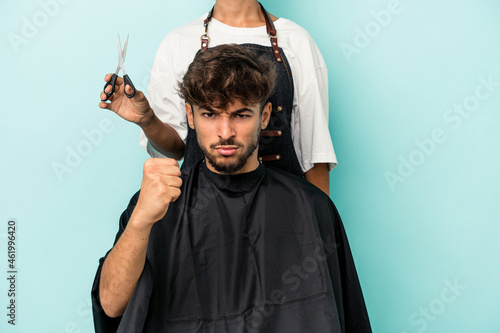 Young arab man ready to get a haircut isolated on blue background showing fist to camera, aggressive facial expression.