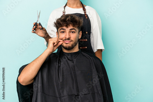 Young arab man ready to get a haircut isolated on blue background with fingers on lips keeping a secret.