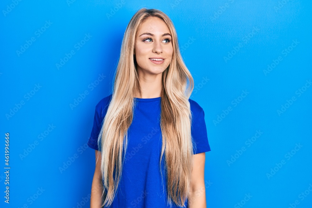 Young beautiful caucasian woman wearing casual blue t shirt looking to side, relax profile pose with natural face and confident smile. Young beautiful caucasian woman wearing casual blue t shirt looking to side, relax profile pose with natural face and confident smile.