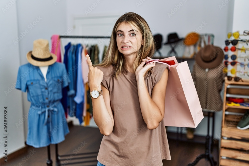 Young blonde woman holding shopping bags at retail shop pointing aside worried and nervous with forefinger, concerned and surprised expression Young blonde woman holding shopping bags at retail shop pointing aside worried and nervous with forefinger, concerned and surprised expression