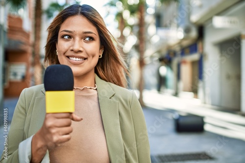 Young latin woman smiling confident using microphone at street