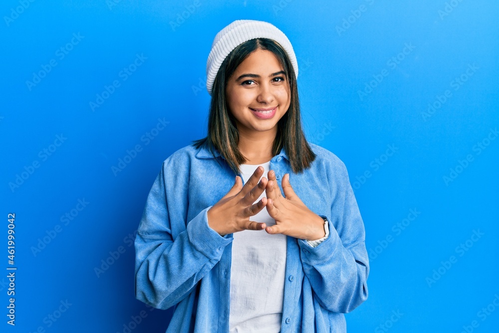 Young latin woman wearing cute wool cap hands together and fingers crossed smiling relaxed and cheerful. success and optimistic Young latin woman wearing cute wool cap hands together and fingers crossed smiling relaxed and cheerful. success and optimistic