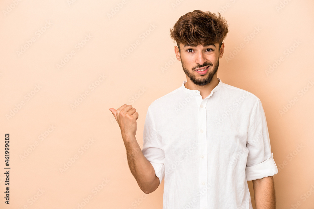 Young arab man isolated on beige background shocked pointing with index fingers to a copy space. Young arab man isolated on beige background shocked pointing with index fingers to a copy space.