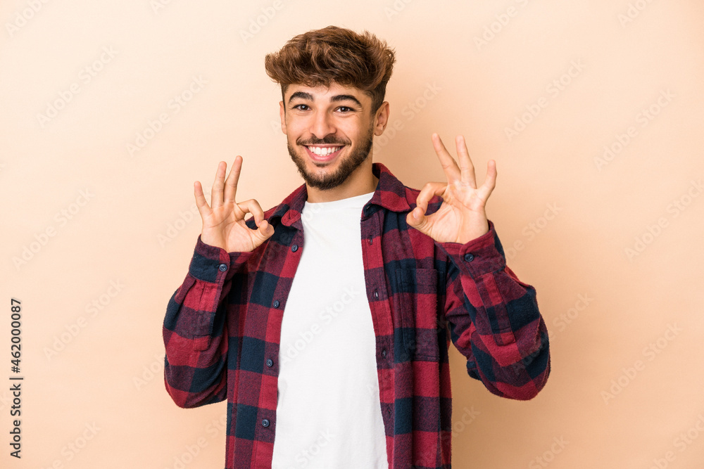 Young arab man isolated on beige background cheerful and confident showing ok gesture. Young arab man isolated on beige background cheerful and confident showing ok gesture.