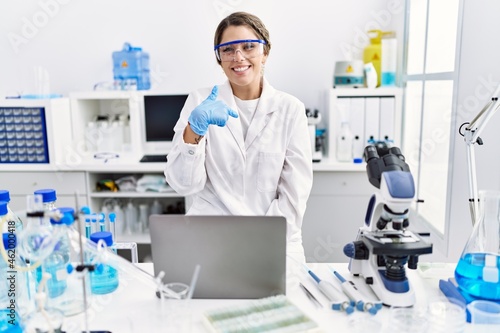 Young hispanic woman wearing scientist uniform working at laboratory pointing finger to one self smiling happy and proud