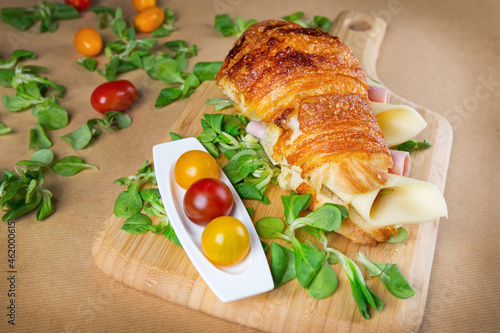 Croissant sandwich filled with ham and cheese on wooden chopping board