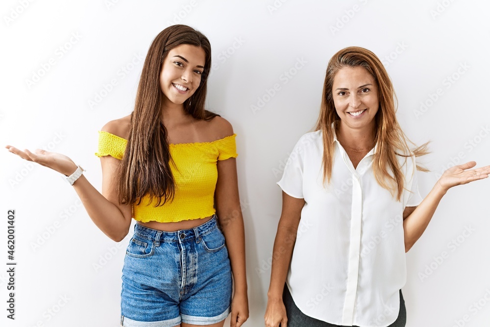 Mother and daughter together standing together over isolated background smiling cheerful presenting and pointing with palm of hand looking at the camera. Mother and daughter together standing together over isolated background smiling cheerful presenting and pointing with palm of hand looking at the camera.