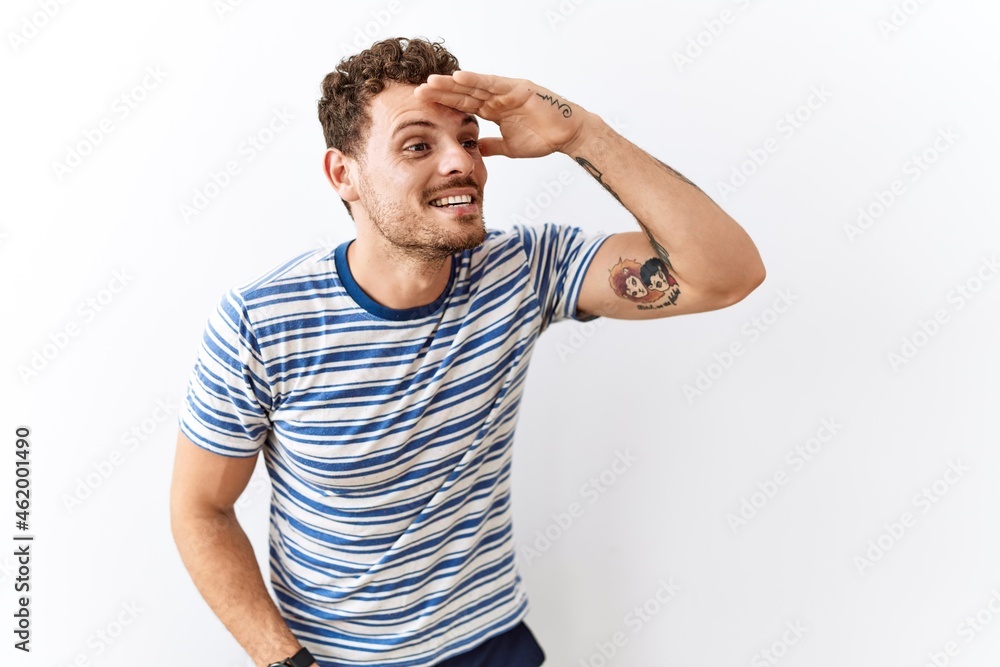 Fototapeta premium Handsome young man standing over isolated background very happy and smiling looking far away with hand over head. searching concept.