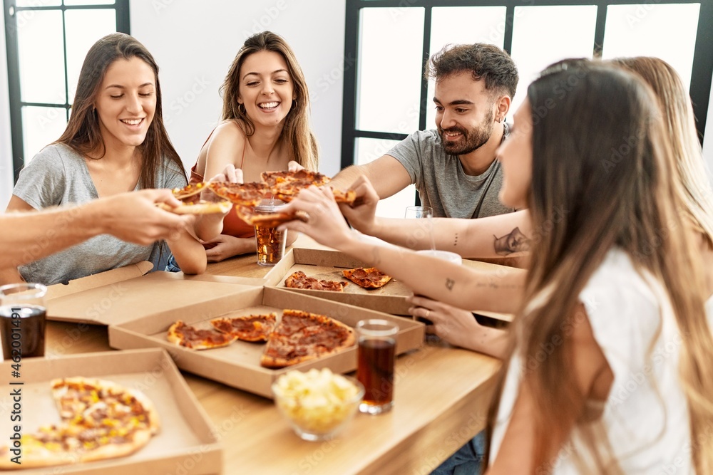 Group of young people smiling happy eating italian pizza sitting on the table at home