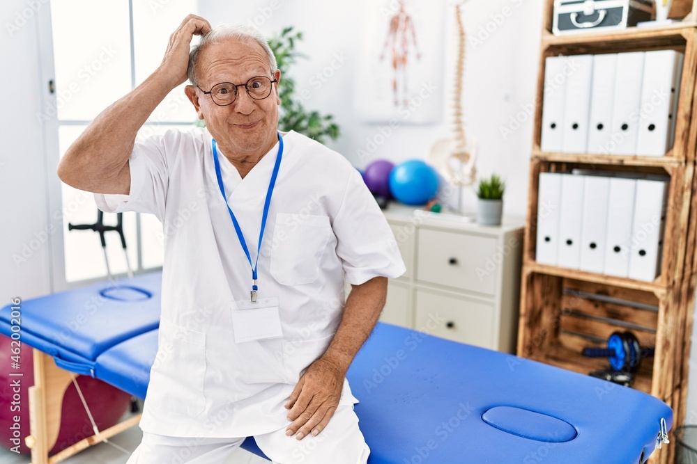 Senior physiotherapy man working at pain recovery clinic confuse and wonder about question. uncertain with doubt, thinking with hand on head. pensive concept. Senior physiotherapy man working at pain recovery clinic confuse and wonder about question. uncertain with doubt, thinking with hand on head. pensive concept.