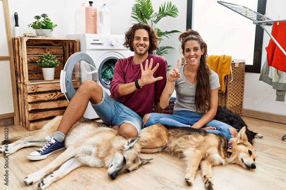Young hispanic couple doing laundry with dogs showing and pointing up with fingers number six while smiling confident and happy.