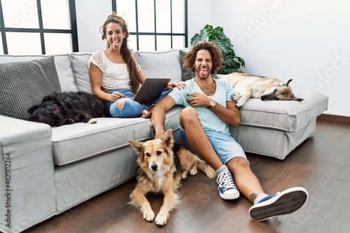 Canvas Print Young hispanic couple with dogs relaxing at home sticking tongue out happy with funny expression
