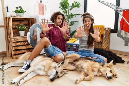 Canvas Print Young hispanic couple doing laundry with dogs afraid and terrified with fear expression stop gesture with hands, shouting in shock