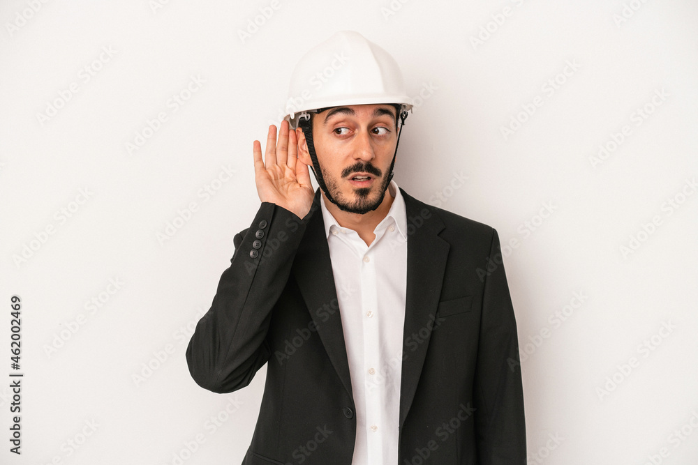Young architect man wearing a construction helmet isolated on white background trying to listening a gossip. Young architect man wearing a construction helmet isolated on white background trying to listening a gossip.
