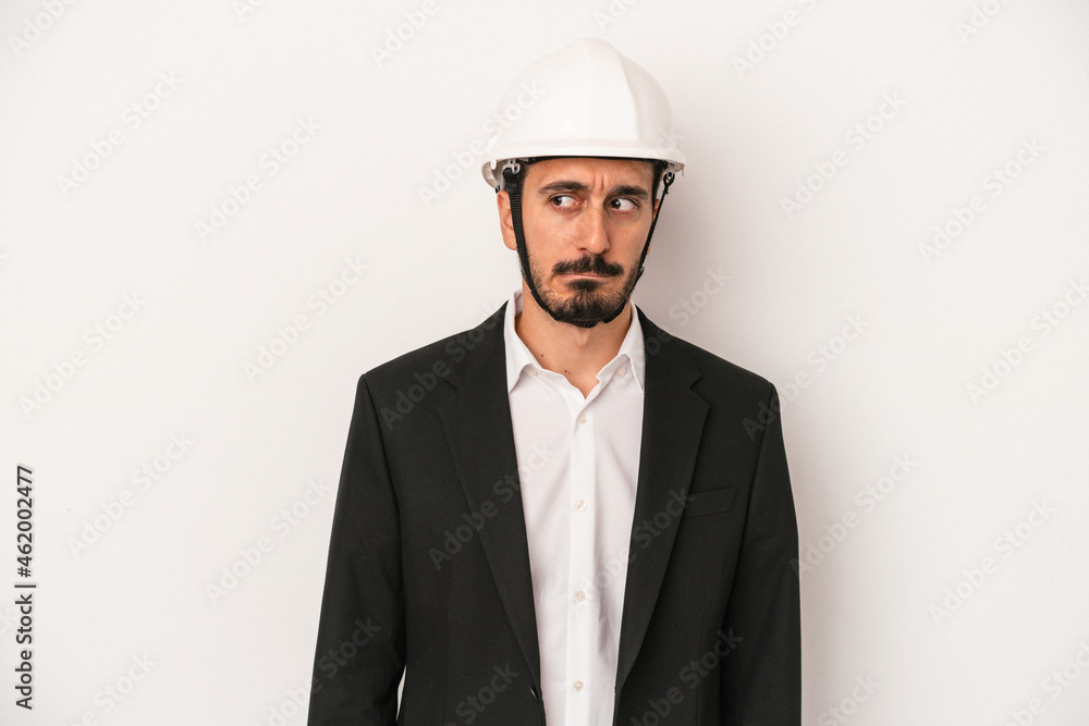 Young architect man wearing a construction helmet isolated on white background confused, feels doubtful and unsure. Young architect man wearing a construction helmet isolated on white background confused, feels doubtful and unsure.
