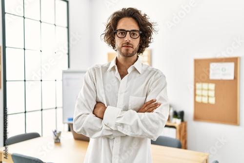 Young hispanic businessman with serious expression standing with arms crossed gesture at office.