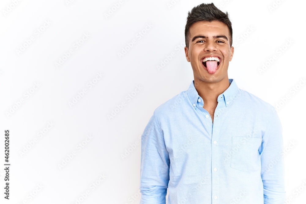 Young hispanic man wearing business shirt standing over isolated background sticking tongue out happy with funny expression. emotion concept. Young hispanic man wearing business shirt standing over isolated background sticking tongue out happy with funny expression. emotion concept.