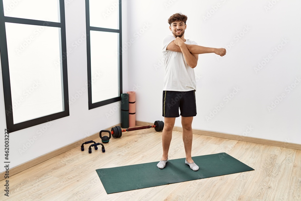 Young arab man smiling confident stretching at sport center