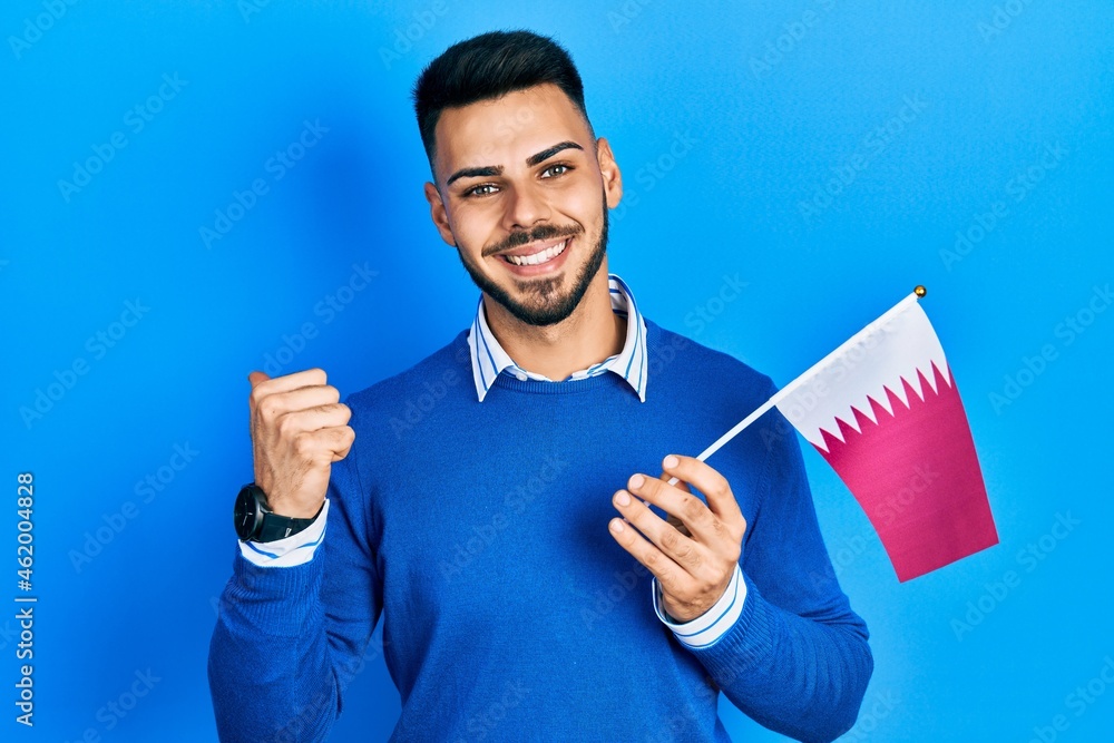 Young hispanic man with beard holding qatar flag pointing thumb up to the side smiling happy with open mouth Young hispanic man with beard holding qatar flag pointing thumb up to the side smiling happy with open mouth