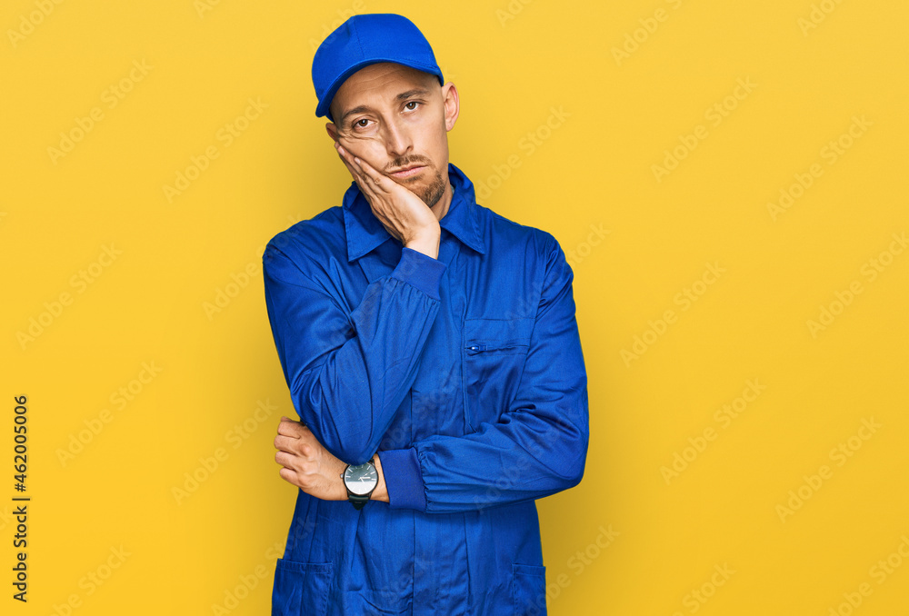 Bald man with beard wearing builder jumpsuit uniform thinking looking tired and bored with depression problems with crossed arms.