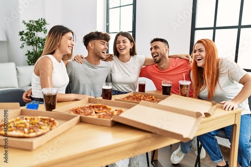 Group of young people smiling happy and hugging eating italian pizza at home.