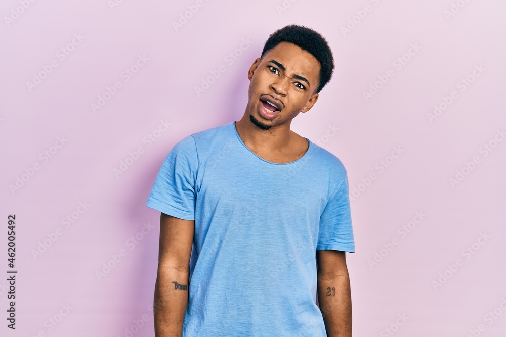 Young african american man wearing casual blue t shirt in shock face, looking skeptical and sarcastic, surprised with open mouth Young african american man wearing casual blue t shirt in shock face, looking skeptical and sarcastic, surprised with open mouth