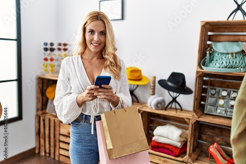 Young blonde woman using smartphone shopping at clothing store