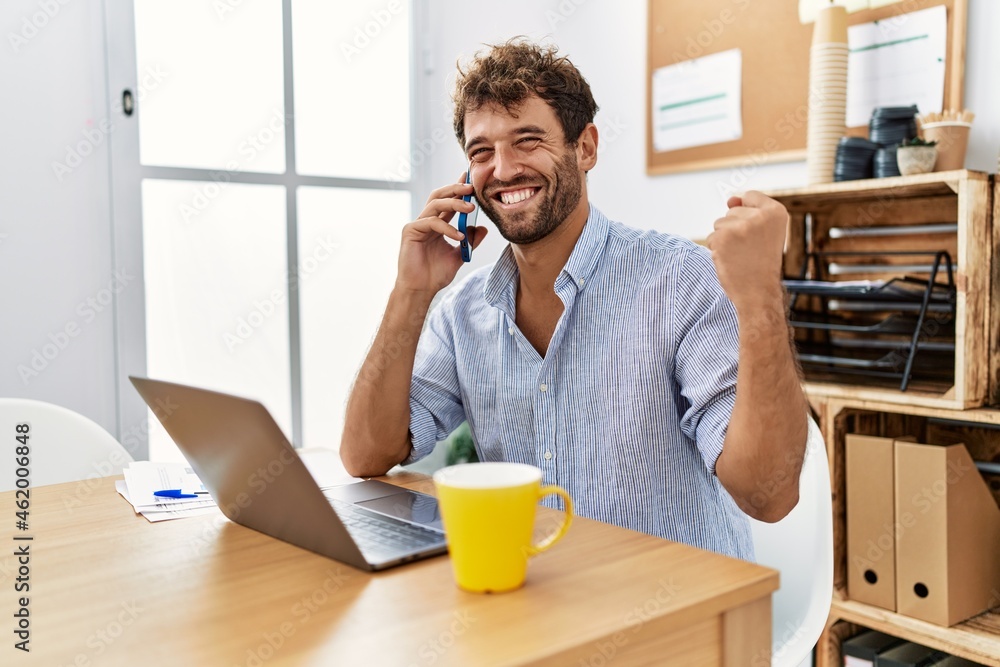 Young handsome man working at the office speaking on the phone screaming proud, celebrating victory and success very excited with raised arm Young handsome man working at the office speaking on the phone screaming proud, celebrating victory and success very excited with raised arm