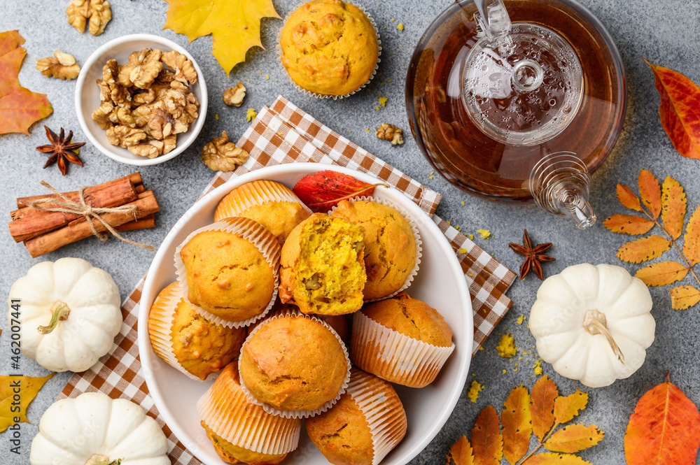 Spicy pumpkin muffins or cupcakes with walnuts in a white plate. Autumn bakery concept. Tea party . Teapot of black tea. Top view Spicy pumpkin muffins or cupcakes with walnuts in a white plate. Autumn bakery concept. Tea party . Teapot of black tea. Top view