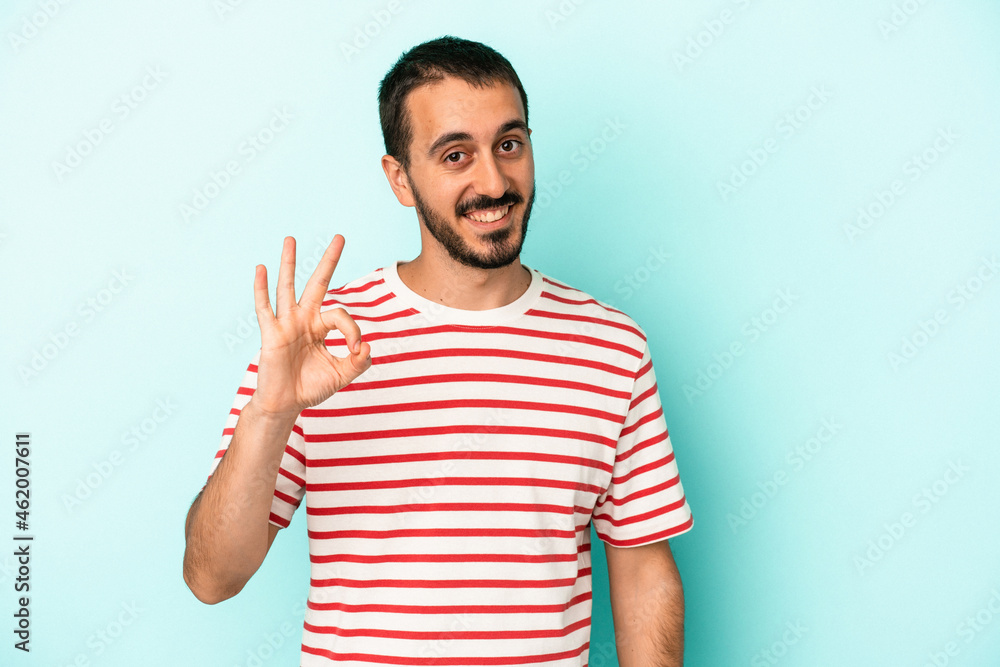 Fototapeta premium Young caucasian man isolated on blue background cheerful and confident showing ok gesture.