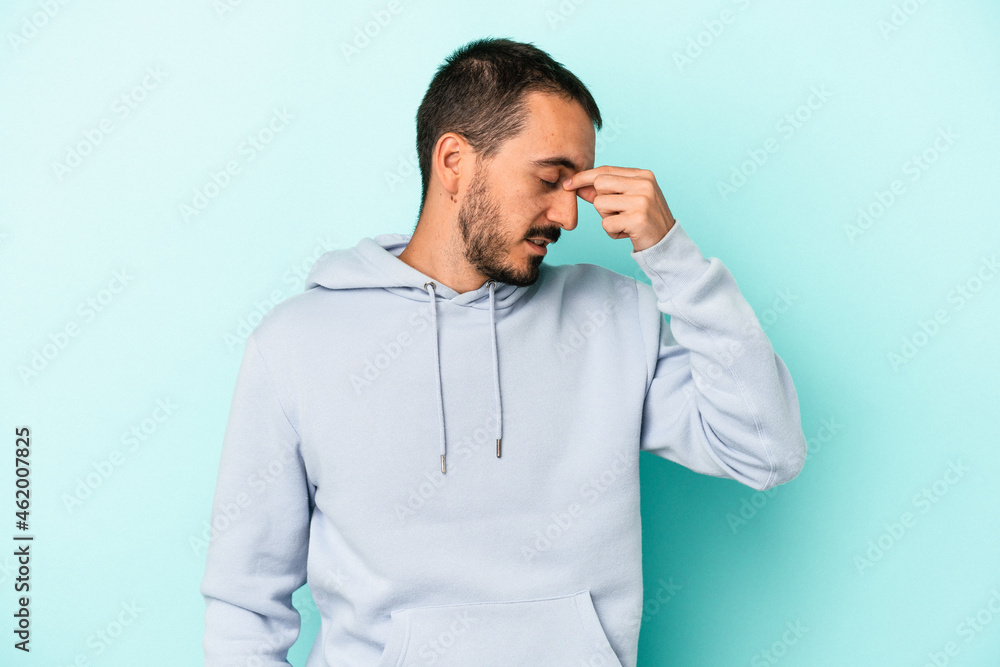 Young caucasian man isolated on blue background having a head ache, touching front of the face. Young caucasian man isolated on blue background having a head ache, touching front of the face.