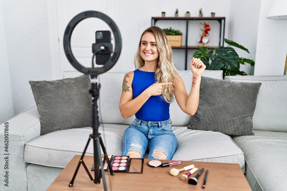 Young beautiful woman recording make up vlog tutorial with smartphone at home smiling happy pointing with hand and finger Young beautiful woman recording make up vlog tutorial with smartphone at home smiling happy pointing with hand and finger