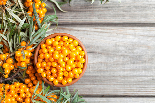 Fresh, juicy, ripe sea buckthorn berries (Hippophae) in clay pot on a wooden background. Top view photo