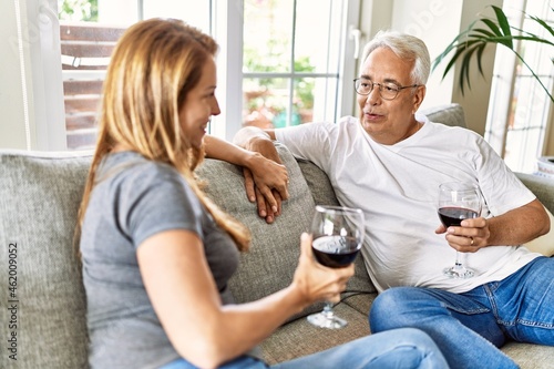 Middle age hispanic couple smiling happy drinking wine sitting on the sofa at home.