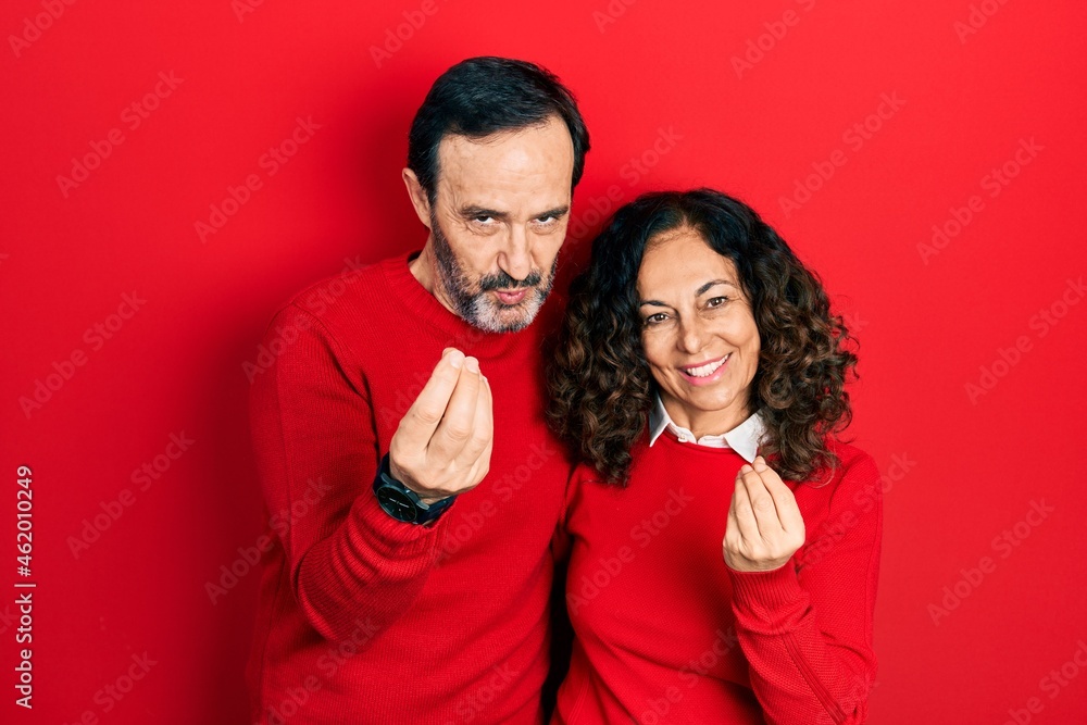 Fototapeta premium Middle age couple of hispanic woman and man hugging and standing together doing money gesture with hands, asking for salary payment, millionaire business