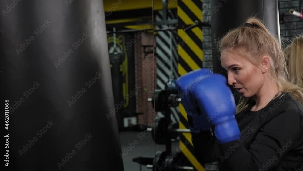 A beautiful young woman in blue boxing gloves hits a punching bag in the gym. Boxing training. A beautiful young woman in blue boxing gloves hits a punching bag in the gym. Boxing training.