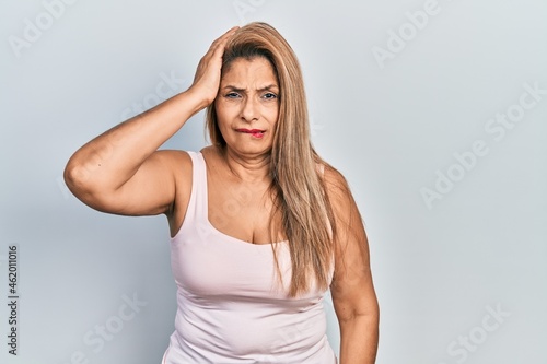 Middle age hispanic woman wearing casual style with sleeveless shirt confuse and wonder about question. uncertain with doubt, thinking with hand on head. pensive concept.